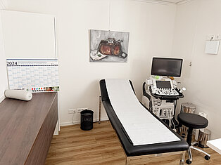 Ultraschallraum im MVZ Goldbach Behandlungsraum im MVZ Goldbach mit Liege, Ultraschallgerät, Hocker und Wandbild einer Arzttasche.