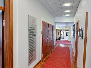 Flur mit Leistungsübersicht im MVZ Goldbach Flur im MVZ Goldbach mit rot gepunktetem Teppich und Übersicht medizinischer Leistungen an der Wand.